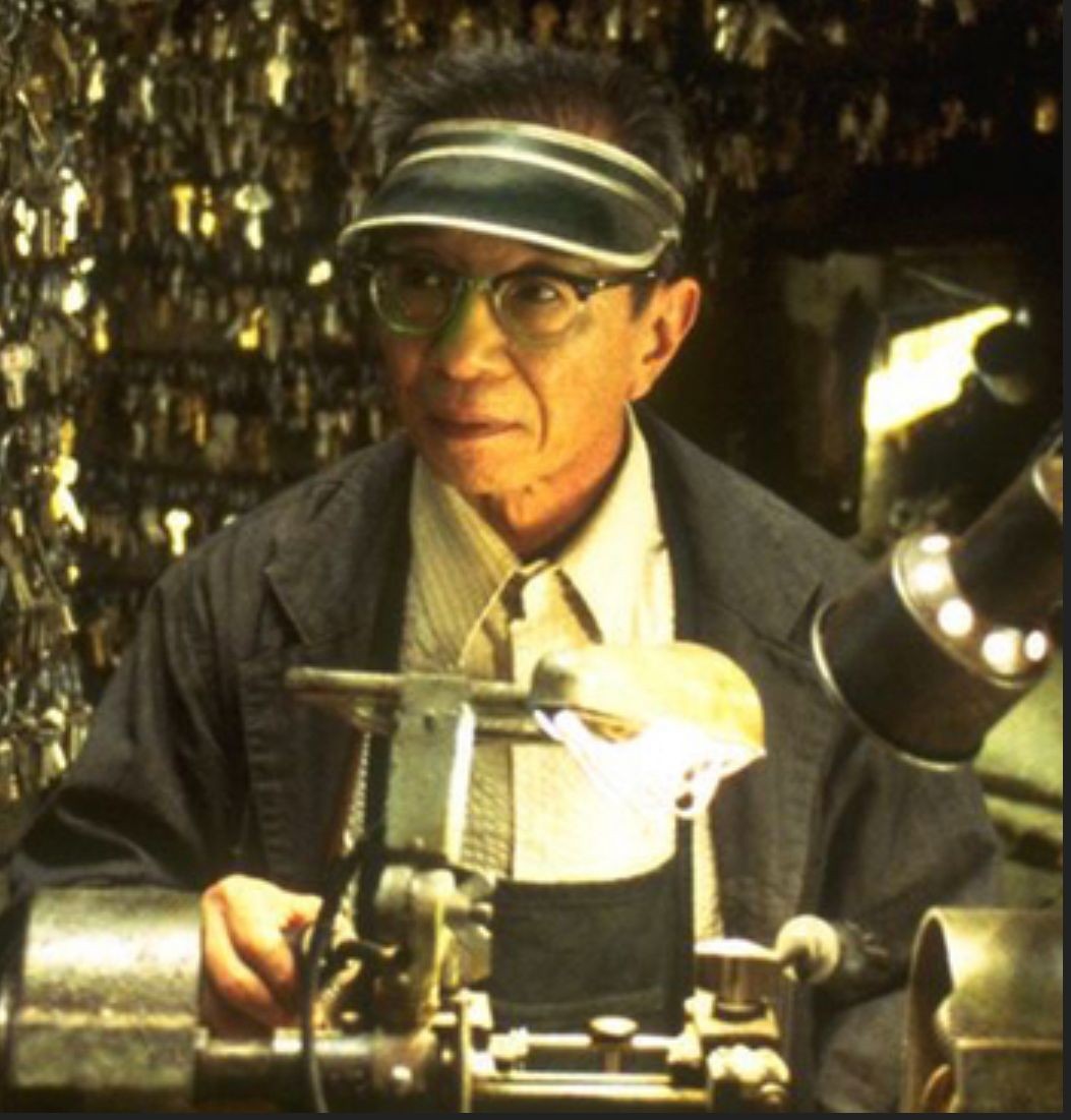 Person working at a key duplication machine, surrounded by numerous hanging keys in a locksmith shop.