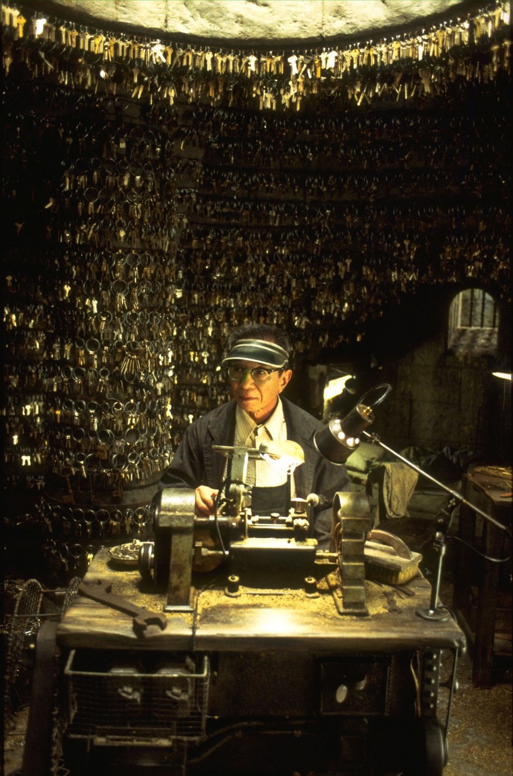 Person working in a cluttered workshop filled with hundreds of keys hanging from the walls and ceiling.